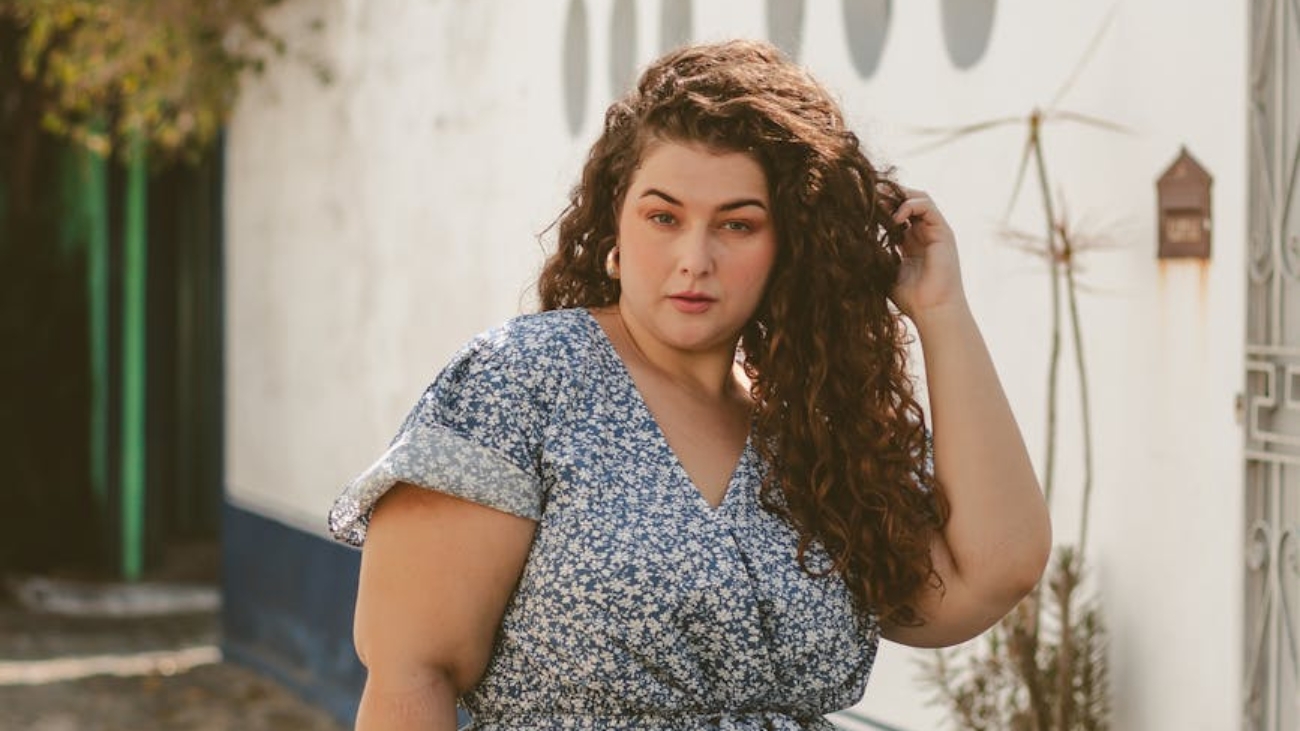 young woman in a blue floral dress standing and fixing her hair