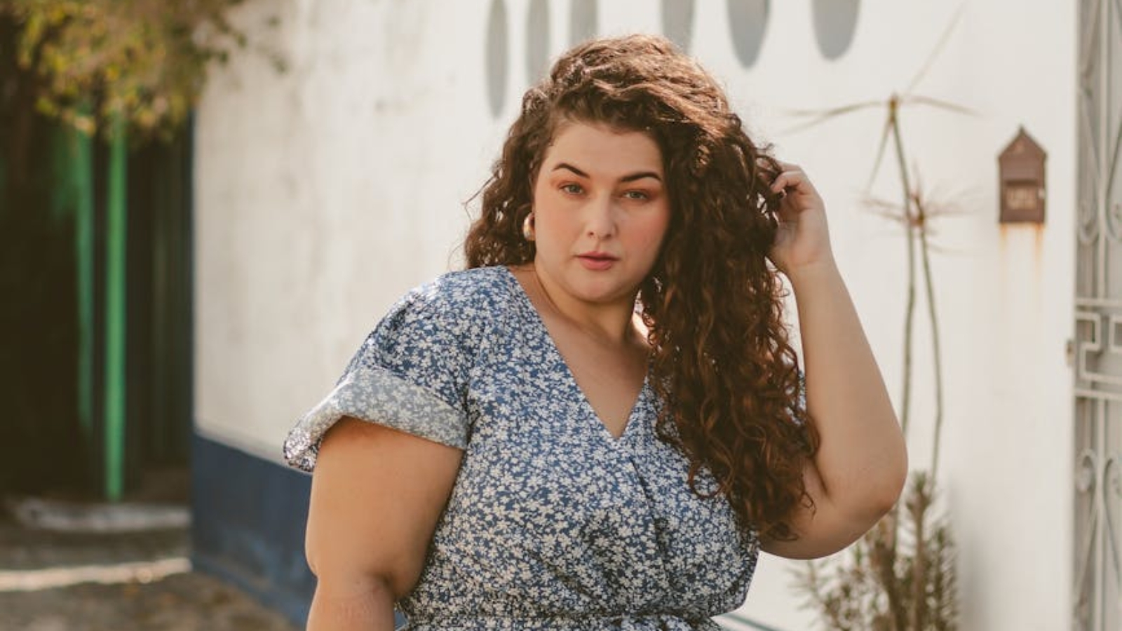 young woman in a blue floral dress standing and fixing her hair