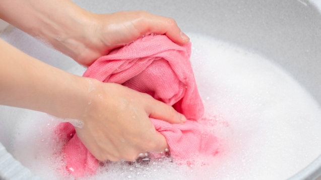 Mãos lavando cuidadosamente peça de roupa delicada em água fria, com sabão neutro, representando cuidados manuais.